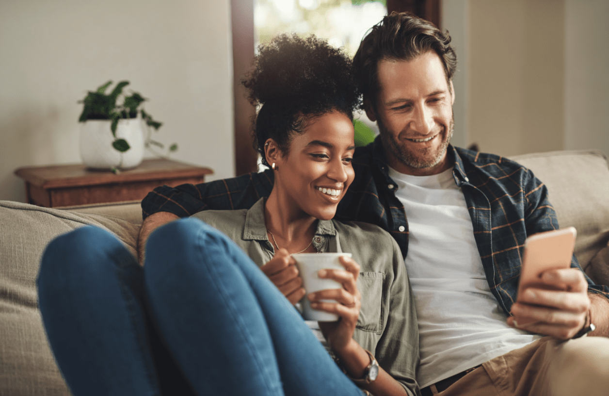 Eine Frau und ein Mann sitzen auf einer Couch und schauen auf ein Smartphone